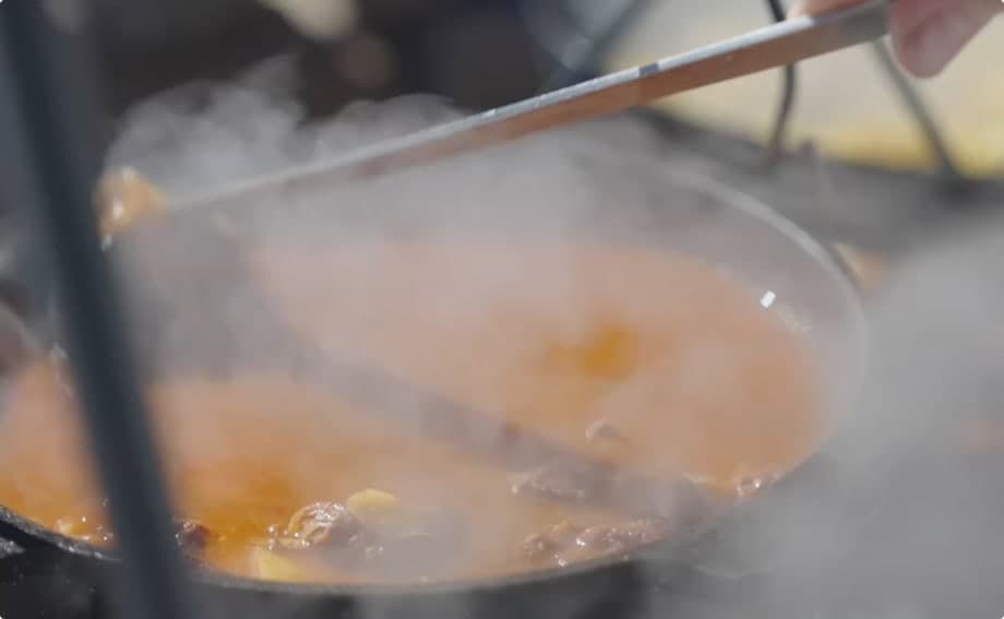 Close-up of stew cooking over heat in a pot with steam rising.