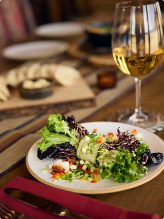 Fresh plated salad with a glass of white wine on a rustic dining table.